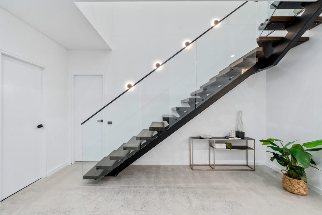 Image shows a well-lit modern home interior with stair case, stone floor and house plants decor