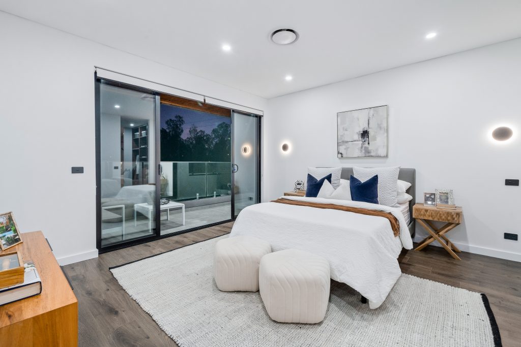 Image shows a large bedroom with balcony. Wooden floors, led lighting. Spacious with white walls. Home built by Benelong Projects Sydney based home builders
