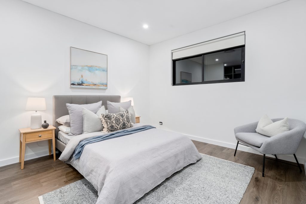 Image shows a spacious bedroom with large windows, white wall, and wooden floor. Sydney based home builders Benelong Projects