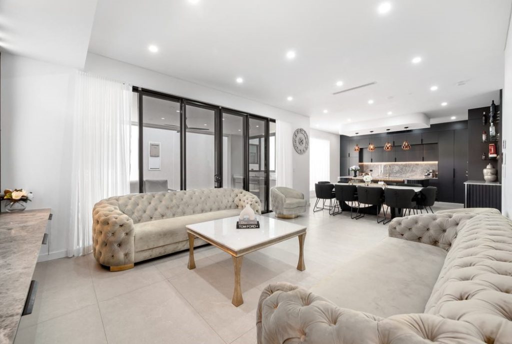 Image shows an open-plan interior design with stone tile floors, comfortable seating and dining area. Granite bench-tops