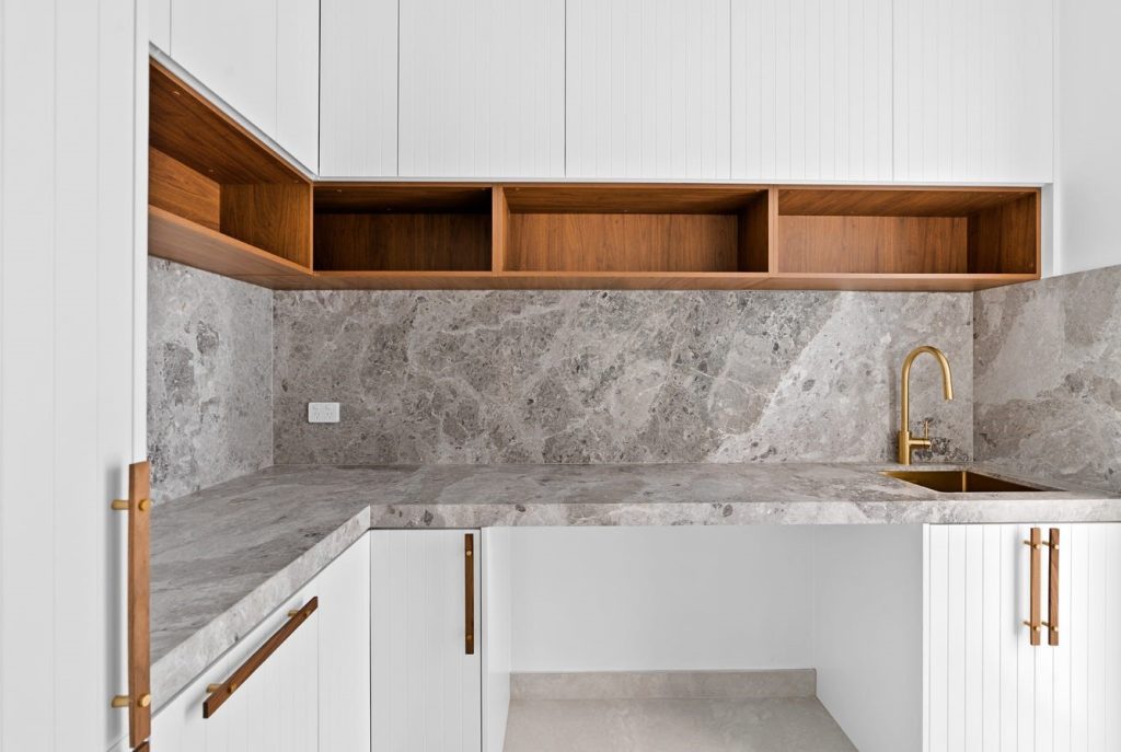 Image shows a food preparation area with stone tiles on the floor, granite bench-tops and brass gold fittings. Custom cupboards and storage. Designed and built by Benelong Projects, Sydney