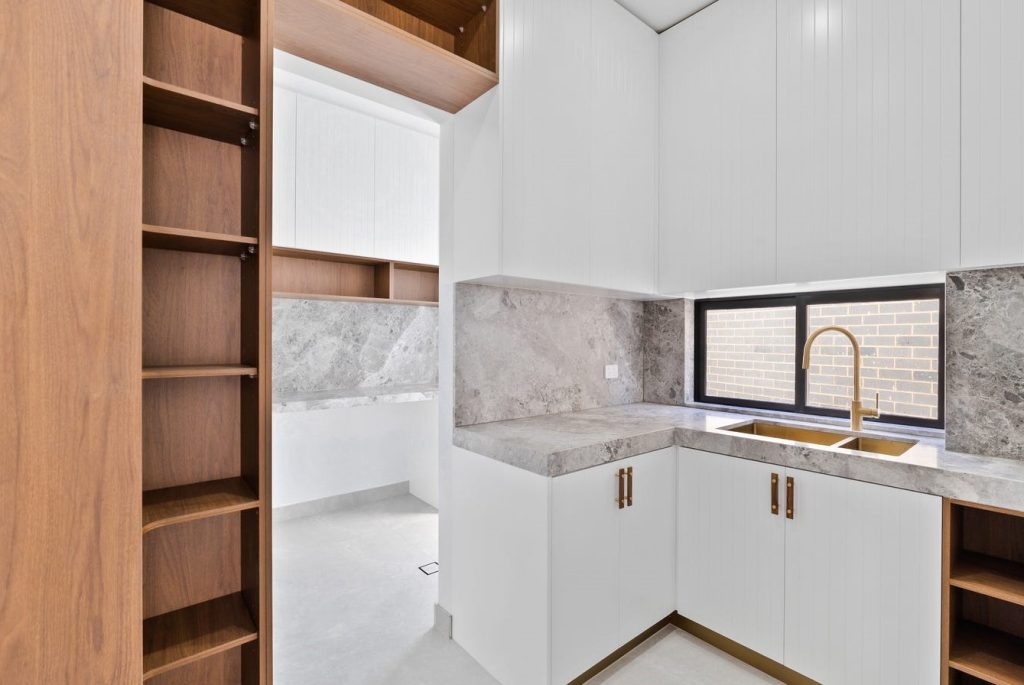 Image shows a second kitchen and preparation area with stone tiles, granite bench-tops, sink, and custom wooden cupboards for storage