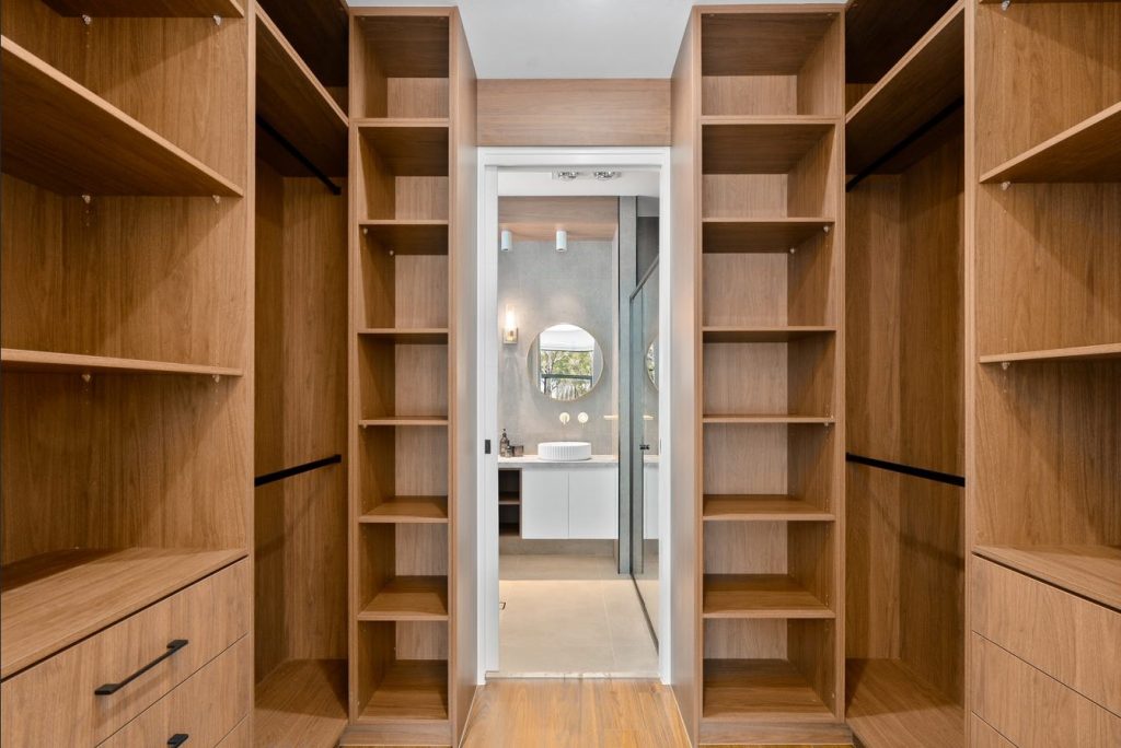 Image shows custom walk-in wardrobes designed and built by Sydney based home builders Benelong Projects. The shelves and drawers and made from wood and are spacious and well-lit