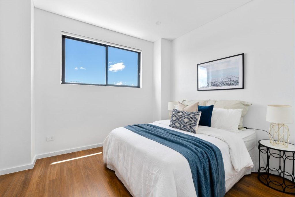 Image shows a well designed bedroom with good natural lighting, large windows, and wooden floors. Spacious bed with side tables and lamps. Home designed and built by Benelong Projects, Sydney based home builders