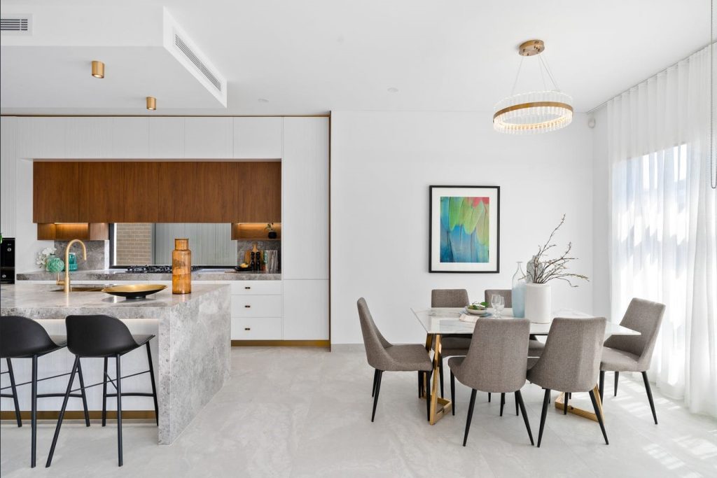 Image shows dining and kitchen area, open-plan. Stone tiled floor with granite bench-tops. Table and chairs for entertaining. Open-plan and well-lit with natural light. Designed and built by Sydney home builders Benelong Projects