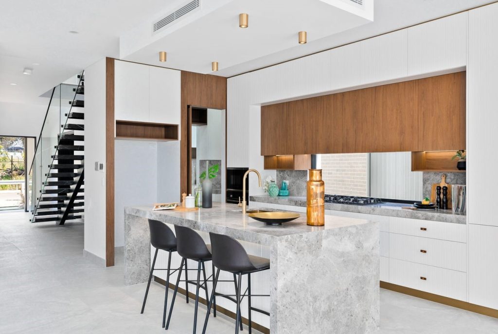 Image shows a modern kitchen with granite bench-top and stone tile floor. Gas cook-top and in-built microwave and oven. Custom cabinetry makes great use of space. Well-lit
