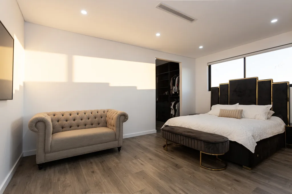 Image shows a well lit and spacious bedroom with wooden floors, a large bed, and a sofa