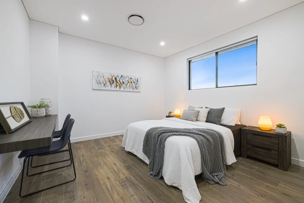 Image shows a large bedroom with large windows, bed, and wooden floors
