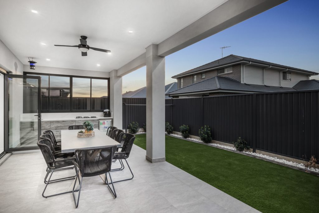 Image shows a Benelong Projects house with spacious outdoor living area, with garden with lush green grass and an outdoor table and chair set. Granite tiled floor