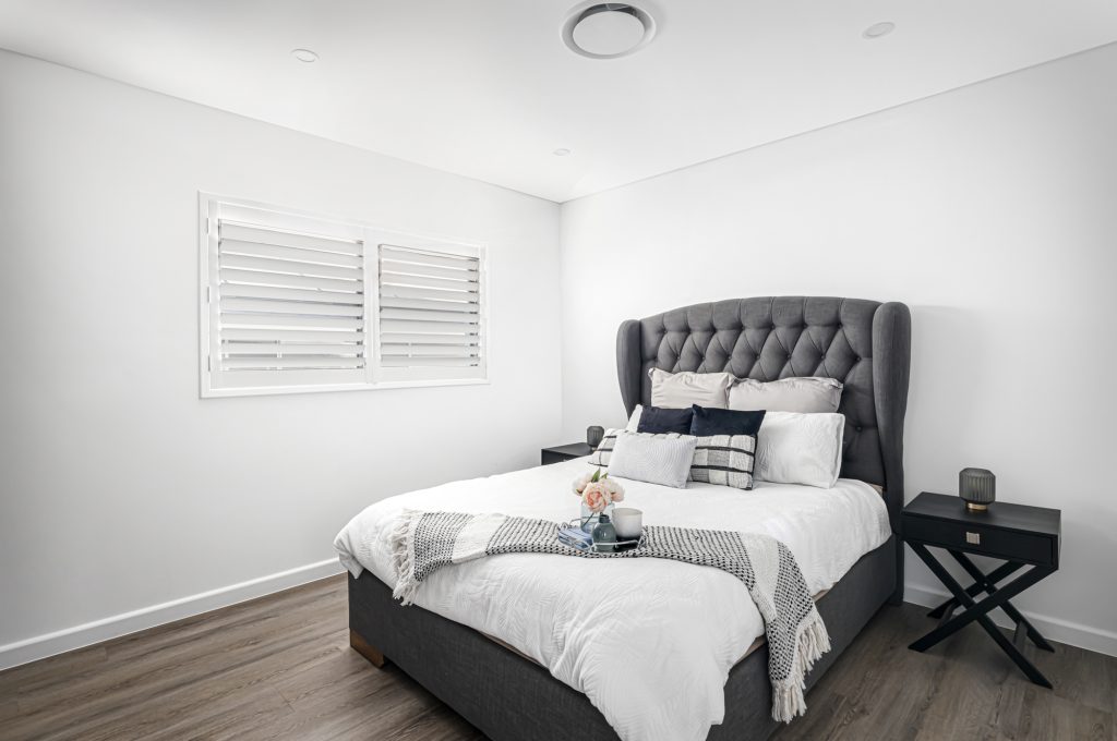 Image shows a modern bedroom with large comfortable bed with side table and wooden flooring