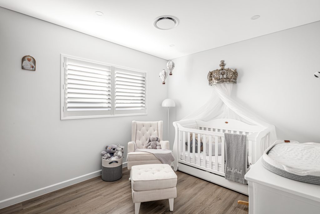 Image shows a spacious child's bedroom with modern interior design. Wooden floors, seating, child's cot