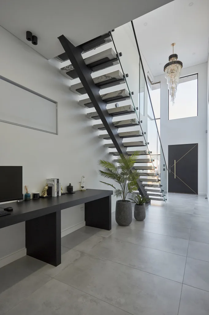Image shows a spacious foyer with white granite staircase, grey tiled floor and chandelier