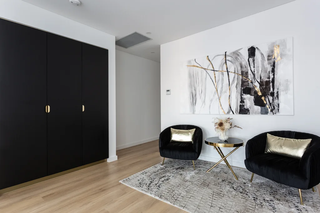 Image shows a spacious indoor area with white walls, wooden floor, and comfortable chairs