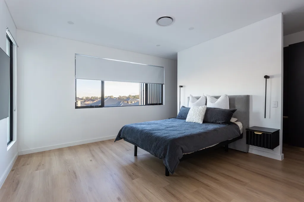 Image shows a spacious, modern, well-lit bedroom with wooden floor and comfortable large bed