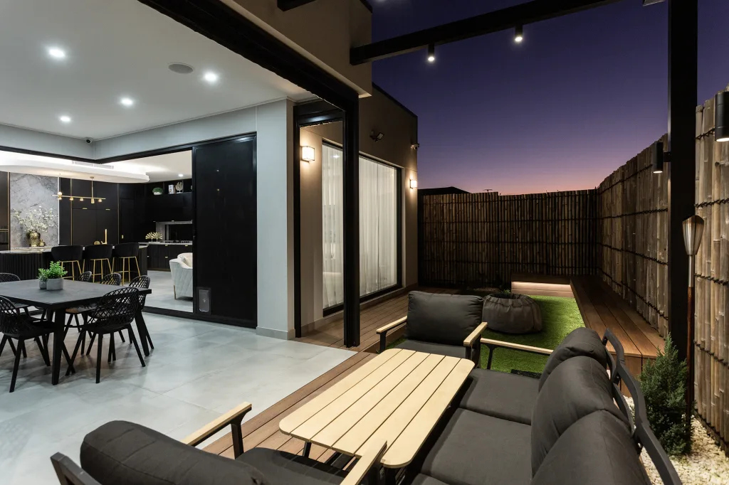 Image shows an outdoor living area with bamboo fence, wooden deck and comfortable table and chairs