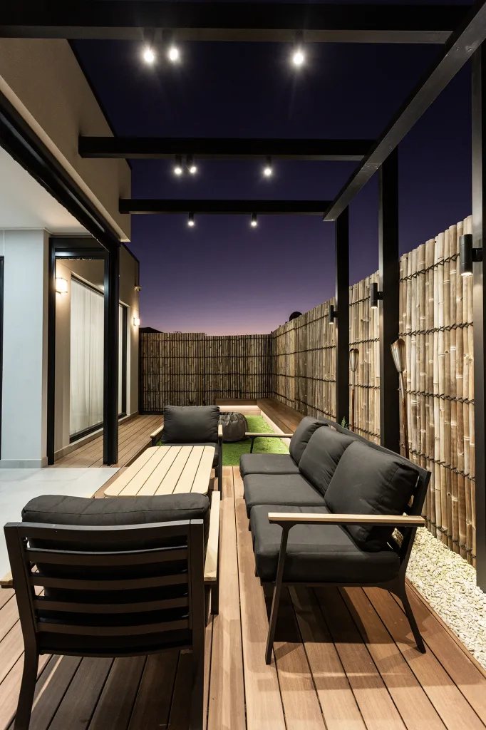 Image shows an outdoor living space with a Japanese theme. Bamboo fence, wooden slat deck and table and chairs