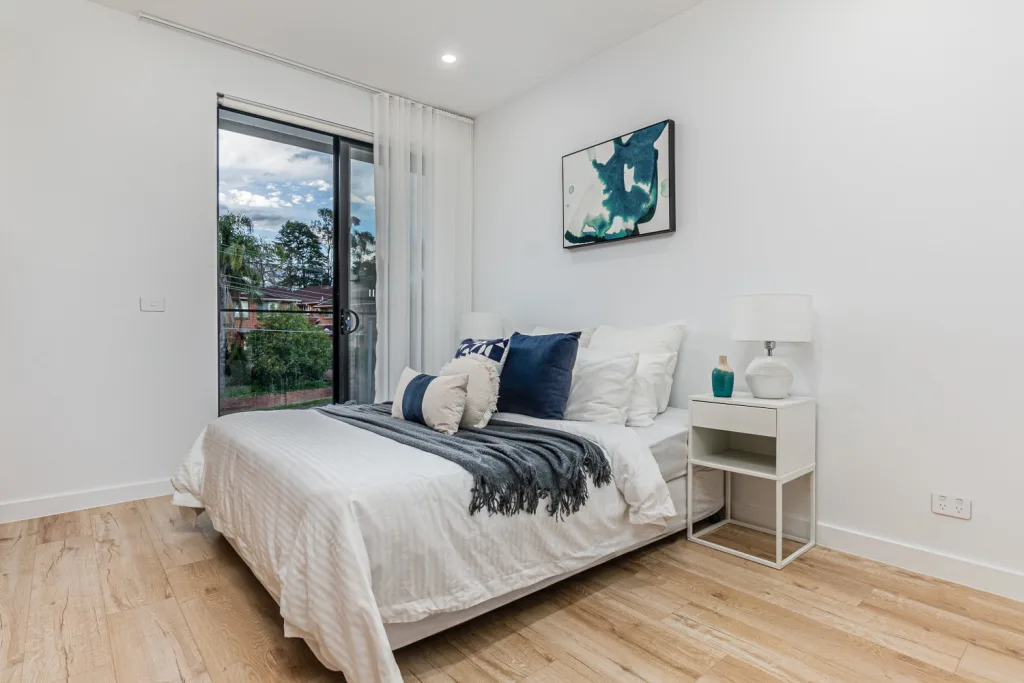Image shows a bedroom with white walls and wooden floors, a large comfortable bed, and a rug on the floor. Built by Benelong Projects Sydney Home Builders
