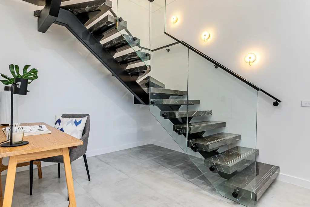 Image shows a house interior with granite stair case with glass safety barrier and grey tiled floors