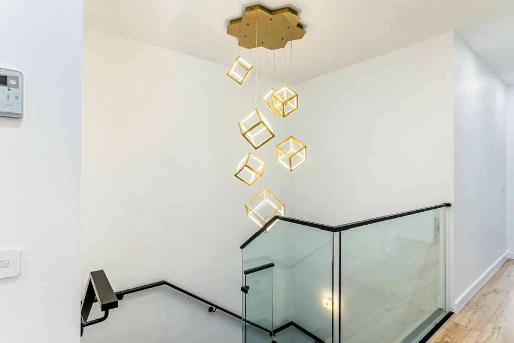 Image shows a house interior with feature lighting, wooden floors, and a glass hand rail/barrier near stairs